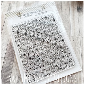 May include: A clear plastic package containing a sheet of photopolymer stamps by SweetMissDaisy Designs, illustrated by Anna Wight. The sheet features a repeating grid of various circular button designs in black ink on a transparent background.