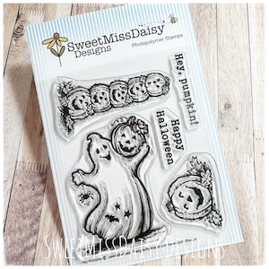 May include: A set of clear photopolymer stamps by SweetMissDaisy Designs featuring a ghost holding a pumpkin, a row of pumpkins, a single pumpkin, and the text Hey, pumpkin! and Happy Halloween. The stamps are arranged on a white backing card.
