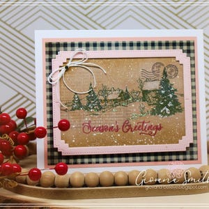 May include: A handmade Christmas card with a winter scene featuring trees, a house, and the text "Season's Greetings." The card has a pink border, a black and white checkered background, and a white bow.