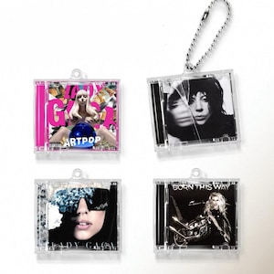 May include: Four clear plastic CD cases with keychains attached. Each case contains a different Lady Gaga album cover: Artpop, Born This Way, The Fame, and a black and white photo of Lady Gaga.