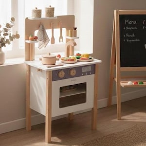 May include: A wooden toy kitchen set with a white and lavender color scheme. The set includes a stove, oven, and accessories like pots, utensils, and toy food. The kitchen is made of wood and has a natural finish, with a small digital clock on the stove.
