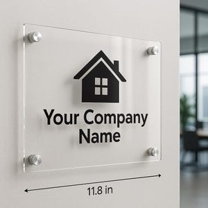 Peut inclure: Panneau en acrylique transparent avec une icône de maison noire et le texte "Your Company Name". Le panneau mesure 30 cm de large et est monté avec quatre entretoises argentées. L'icône de la maison a un toit, une cheminée et quatre fenêtres.