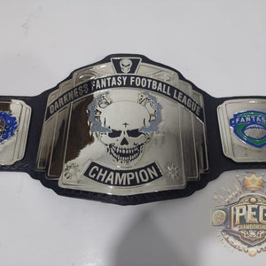 Könnte beinhalten: Ein silberner Meisterschaftsgürtel mit einem schwarzen Lederriemen. Die Mittelplatte zeigt einen Schädel mit einem Kreuz und den Text "Darkness Fantasy Football League Champion".