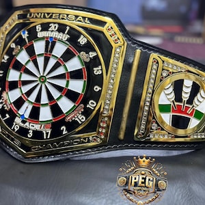 May include: A black and gold championship belt featuring a dartboard design in the center. The belt has the text "UNIVERSAL" and "CHAMPION" on it. The belt also has a logo that says "PEG CHAMPIONSHIP".