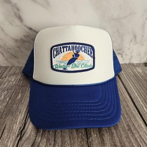 May include: A white and blue trucker hat with a patch that says "Chattahoochee Water Ski Club" with a graphic of a person water skiing in front of a sunset.