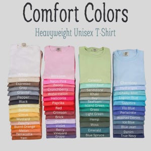 May include: Four stacks of Comfort Colors Heavyweight Unisex T-Shirts in various colors. Each shirt is labeled with its specific color name, including White, Ivory, Espresso, Gray, Granite, Pepper, Black, Banana, Butter, Citrus, Mustard, Peachy, Burnt Orange, Melon, Terracotta, Yam, Blossom, Neon Pink, Peony, Crunchberry, Watermelon, Heliconia, Paprika, Red, Crimson, Brick, Orchid, Violet, Berry, Vineyard, Grape, Celedon, Island Reef, Sandstone, Khaki, Bay, Seafoam, Island Green, Grass, Light Green, Hemp, Moss, Emerald, Blue Spruce, Chambray, Hydrangea, Chalky Mint, Lagoon Blue, Sapphire, Flo Blue, Periwinkle, Washed Denim, Ice Blue, Blue Jean, Denim, and True Navy.