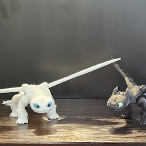 May include: Two dragon figurines, one white and one black, with wings and tails. The white dragon has blue eyes and is facing the left. The black dragon has green eyes and is facing the right.