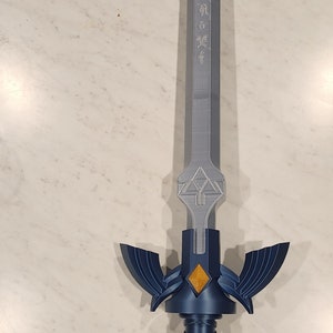 May include: A blue and silver Master Sword replica with a detailed handle and a Triforce symbol on the blade. The blade is inscribed with Hylian characters.