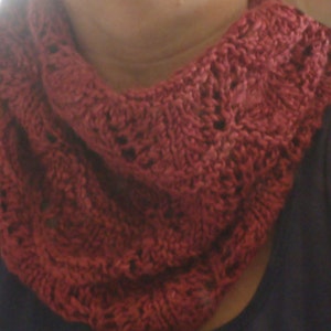 May include: A close-up of a red knitted scarf with a lacy pattern. The scarf is worn around the neck of a person.