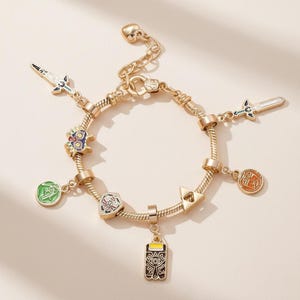 May include: Gold-toned charm bracelet featuring various enamel charms. Charms include swords, a shield, and other symbols. The bracelet has a lobster clasp closure and a heart-shaped charm at the end of the chain.