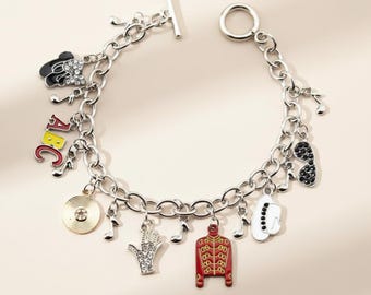 May include: Silver charm bracelet featuring music-themed charms. Charms include musical notes, a record, a hand, and a red and gold jacket. The bracelet has a toggle clasp and is suitable for everyday wear.