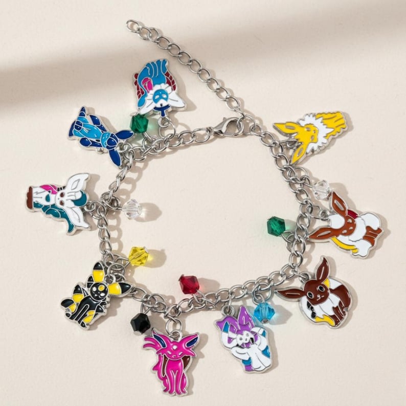 May include: A silver charm bracelet with colourful enamel charms depicting cartoon characters. The charms are in shades of blue, yellow, pink, and brown, with small, colourful beads along the chain.
