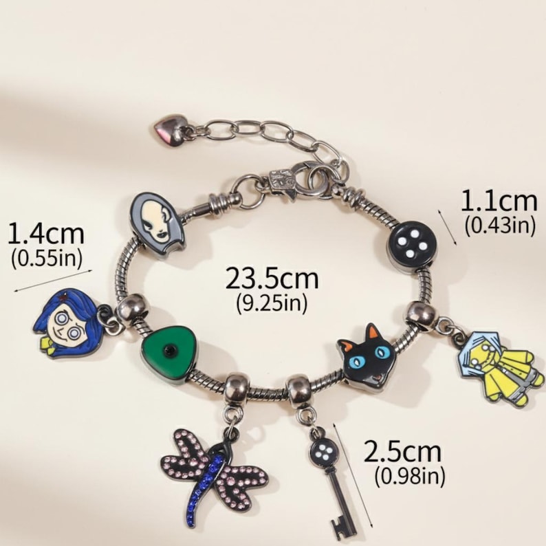 May include: A silver-toned charm bracelet featuring colorful enamel charms. The bracelet includes charms of a girl, a cat, a key, a dragonfly, a button, and a character with a pale face. The bracelet is 9.25 inches long.