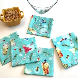 May include: Five turquoise blue fabric coasters with a cocktail theme. The coasters feature a variety of cocktails, including a martini, a margarita, a daiquiri, and a tiki drink. The coasters are perfect for adding a touch of fun to your bar or dining table.