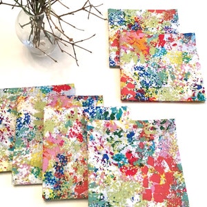 May include: Set of eight colorful napkins with a splatter paint design. The napkins are white with a variety of colors including pink, blue, green, yellow, and red.
