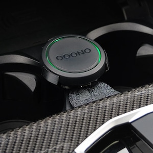 Puede incluir: Un interior de coche negro con un portavasos y un soporte de teléfono negro y verde con la palabra "OOONO" en él.