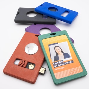 May include: A collection of colorful ID badge holders and accessories. Includes a green and orange badge with a photo and text, a red holder with a USB drive, and several solid-colored holders in blue, black, and purple.