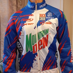 Pode incluir: Uma jaqueta de ciclismo branca, azul e vermelha com o logotipo da Mountain Dew e vários patrocinadores, incluindo Specialized, Shimano, Mavic, Rock Shox, DT Swiss e Bicycle Line.