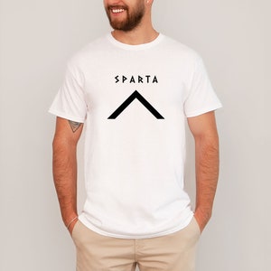 Könnte beinhalten: Weißes T-Shirt mit einer schwarzen Grafik eines Dreiecks und dem Wort "SPARTA" auf der Vorderseite.