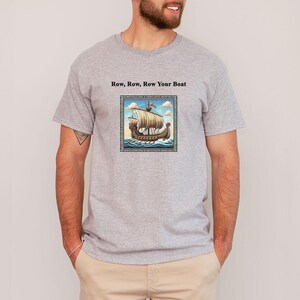 Könnte beinhalten: Ein graues T-Shirt mit dem Aufdruck "Row, Row, Row Your Boat" auf der Vorderseite. Das Shirt zeigt eine Vintage-Illustration eines Schiffes mit Segeln.