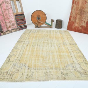May include: A vintage, off-white rug with a faded floral pattern. The rug has a distressed look and a subtle, light yellow hue.