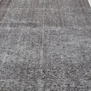 May include: A large, rectangular, distressed-look rug in shades of gray and brown. The rug features an intricate, faded floral pattern and a distressed border. The rug is suitable for a living room or bedroom.