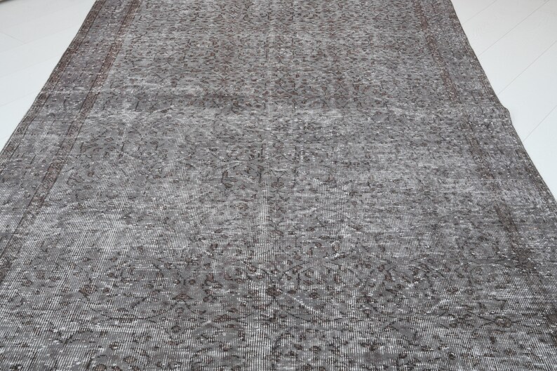 May include: A large, rectangular, distressed-look rug in shades of gray and brown. The rug features an intricate, faded floral pattern and a distressed border. The rug is suitable for a living room or bedroom.
