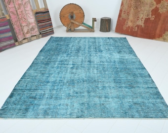May include: A large, rectangular, turquoise rug with a distressed, vintage appearance. The rug has a faded, mottled pattern and is placed on a white floor. The rug is a decorative floor covering.