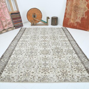 May include: A vintage cream-colored rug with a floral pattern in shades of brown. The rug has a border with a more intricate design.