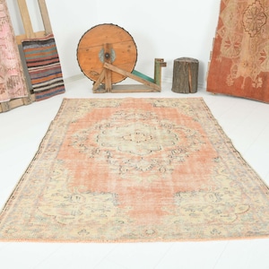 May include: A rectangular area rug featuring a central medallion design in shades of peach, cream, and muted blue. The rug has a distressed appearance with a repeating floral pattern and a wide border, laid flat on a white floor surface.