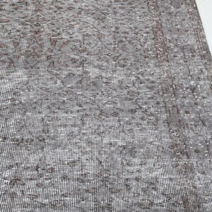 May include: A section of a gray and brown patterned rug. The rug has a distressed, vintage look with a detailed floral design. The rug's color palette includes shades of gray, brown, and white, creating a neutral and versatile aesthetic.