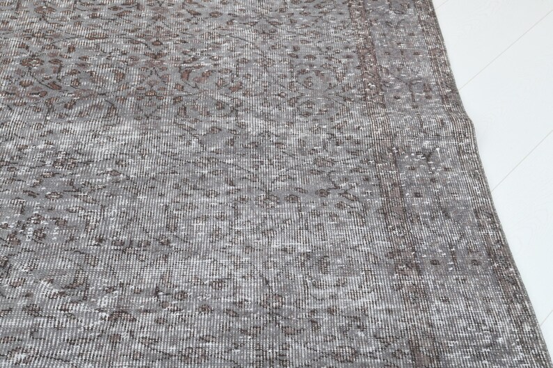 May include: A section of a gray and brown patterned rug. The rug has a distressed, vintage look with a detailed floral design. The rug's color palette includes shades of gray, brown, and white, creating a neutral and versatile aesthetic.
