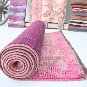 May include: A rolled up pink and purple rug with a brown fringe. The rug is partially unrolled, revealing a pink and beige patterned design.