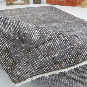 May include: A gray and white patterned rug with a distressed look. The rug is folded over, revealing the underside with a white fringe. The rug has a vintage or antique aesthetic.