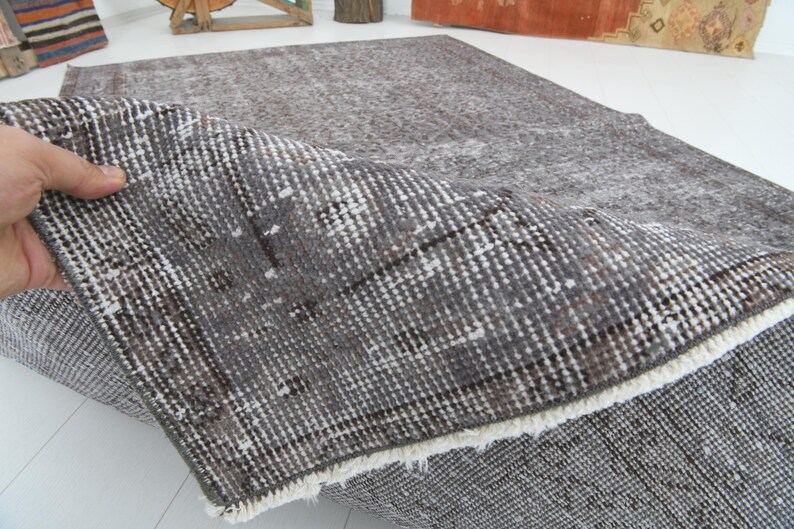 May include: A gray and white patterned rug with a distressed look. The rug is folded over, revealing the underside with a white fringe. The rug has a vintage or antique aesthetic.
