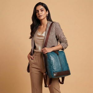 Peut inclure: Un sac à dos bleu sarcelle avec une base en similicuir marron foncé et des bretelles assorties. Le sac présente un compartiment avant zippé vertical, des poches latérales et des détails en métal doré. Il possède une forme rectangulaire.