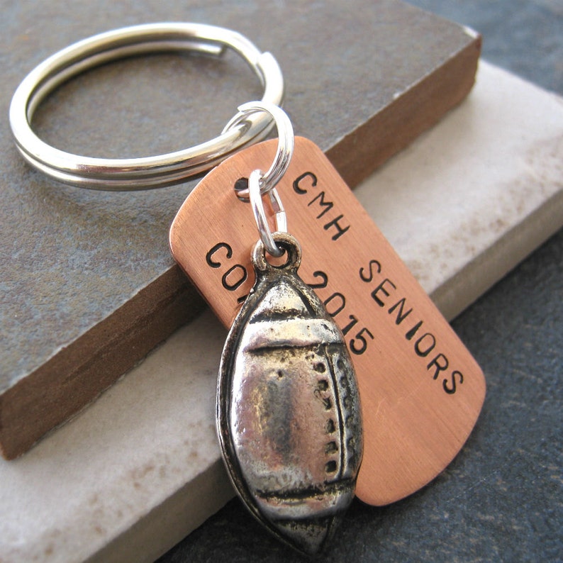 May include: Copper keychain with a silver football charm. The keychain has the text "CMH Seniors 2015" engraved on it.