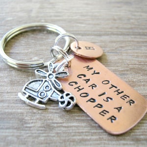 May include: A copper keychain with the text "My other car is a chopper" and a small silver helicopter charm. The keychain also has a small copper charm with the letter "H" on it.
