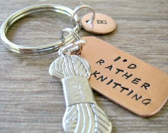 May include: A silver-colored keychain with a yarn spool charm and a copper tag that reads "I'd Rather Knitting." The keychain also includes a small, round charm with the letter "B."