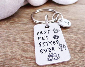 May include: Silver keychain with a tag that reads "Best Pet Sitter Ever" with paw prints and a dog and cat illustration. The keychain also has a small silver charm with the letter "A" on it.