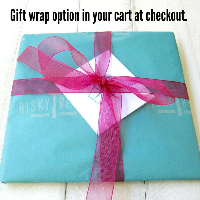 May include: A teal gift box with a pink ribbon tied in a bow. The box has the words "Risky Be" printed on it.