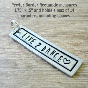 May include: A silver rectangle keychain with a pewter border. The keychain measures 1.75 inches by 0.5 inches and has the text "LIVE 2 DANCE" engraved on it with a heart symbol.