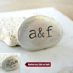 May include: A silver metal charm with the initials "a&f" engraved on the front. The back of the charm has an anniversary date engraved with arrows pointing to the date "12.03.96".
