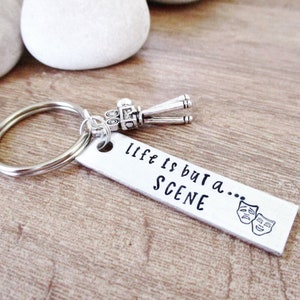 May include: Silver keychain with a small movie clapper charm and a rectangular tag that reads "life is but a... SCENE" with two theater masks.