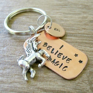 May include: A copper keychain with a silver unicorn charm and the text "I Believe in Magic" with two stars. The keychain also has a small copper tag with the letter "R" on it.
