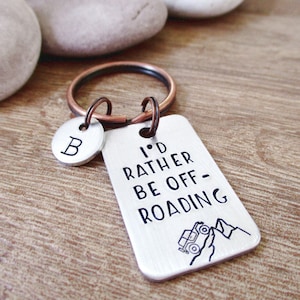 May include: Silver keychain with a charm that says "I'd rather be off-roading" with a small jeep illustration and mountains. The keychain also has a silver charm with the letter "B" on it.