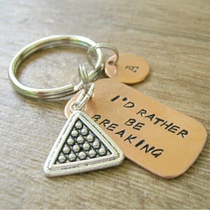 May include: A silver keychain with a copper tag that reads "I'd rather be breaking". The keychain also has a silver charm shaped like a triangle with a pattern of small circles.
