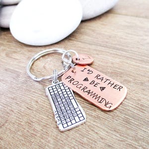 May include: A silver and copper keychain with a silver keyboard charm and a copper tag that reads "I'd Rather Be Programming".