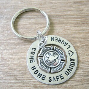 May include: Silver keychain with a round charm that says "Come Home Safe Daddy" with a heart and the name "Lauren". A smaller silver charm with a fire department symbol is in the center.