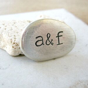 May include: A silver metal charm with the letters "a & f" engraved on it.